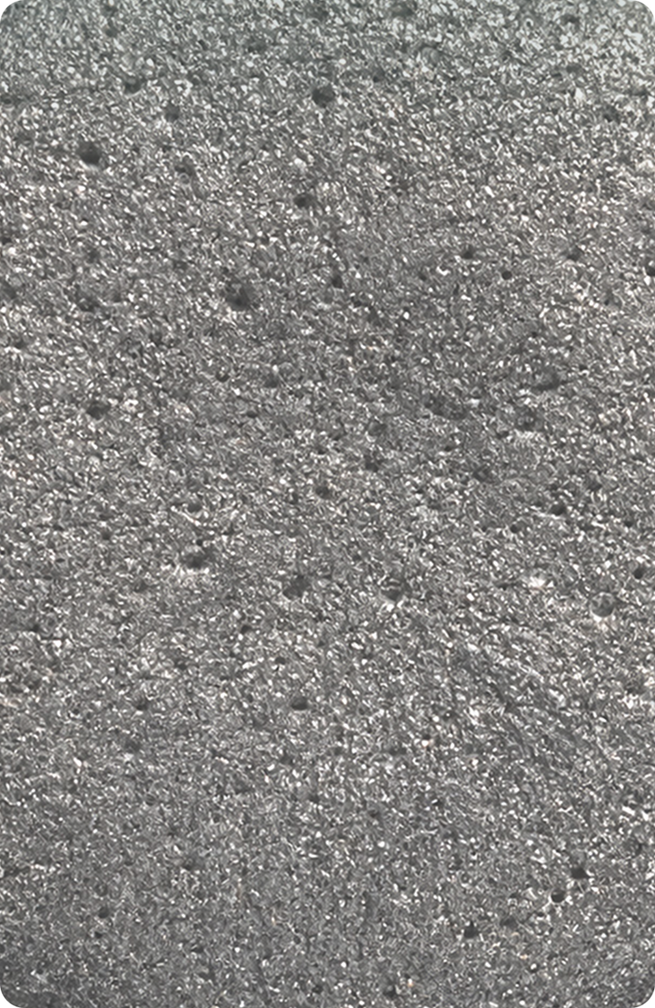 A close-up of a rough, shiny gray metallic surface with small holes and an uneven, bumpy texture throughout.