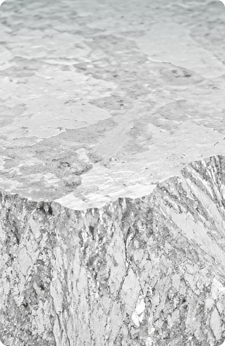 A close-up view of a rough, silver metallic surface with jagged edges and textured patterns, resembling an unpolished chunk of metal or mineral.
