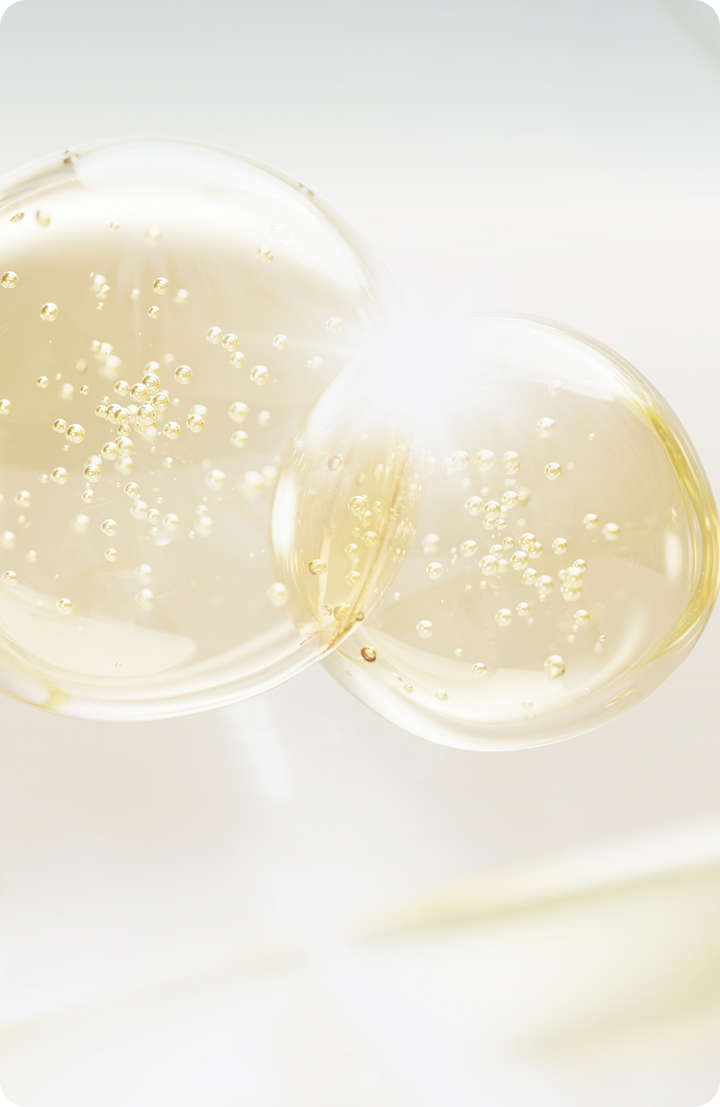 Two translucent golden bubbles with small suspended particles float against a soft white and light background, with bright light reflecting off their surfaces.