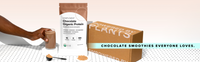 A hand holds a glass of chocolate smoothie beside a bag of Complement Chocolate Organic Protein, powder scoop, and a box labeled Powered by Plants. Text reads: Chocolate smoothies everyone loves..