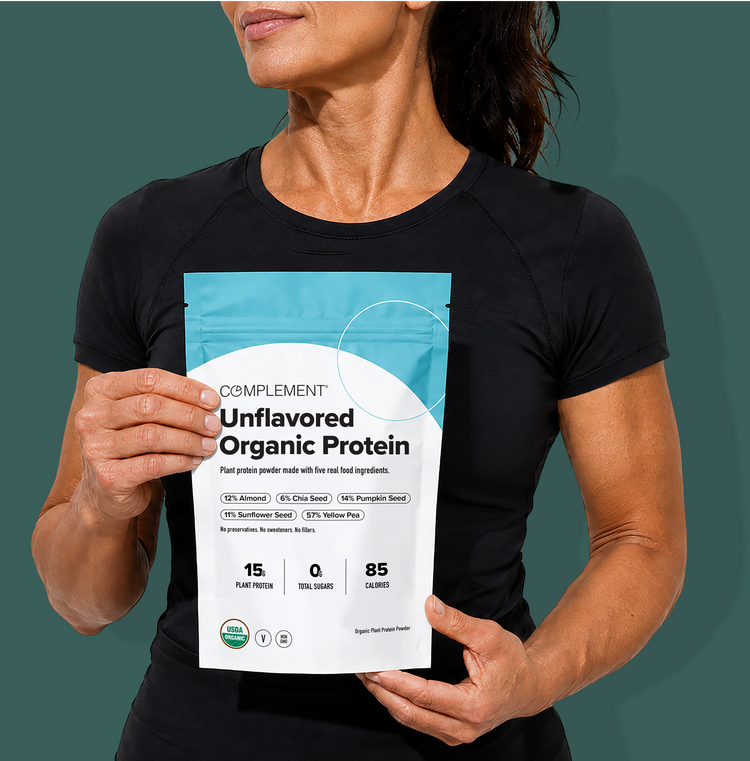A person in a black shirt holds a bag of Complement Unflavored Organic Protein powder, highlighting its plant-based ingredients, 15g protein, 0g sugar, and 85 calories per serving.