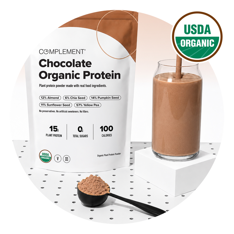 A bag of Complement Chocolate Organic Protein powder, a glass of chocolate protein shake, and a scoop of powder on a white surface with a USDA Organic label in the corner.