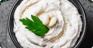 A bowl of creamy white bean dip garnished with whole white beans, a parsley leaf, and sprinkled with sesame seeds on top.