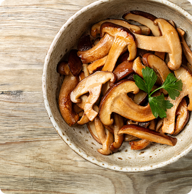 A ceramic bowl filled with cooked sliced mushrooms, garnished with a sprig of parsley, sits on a wooden surface.