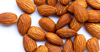 A close-up of several raw almonds with brown, textured shells, scattered on a white surface.