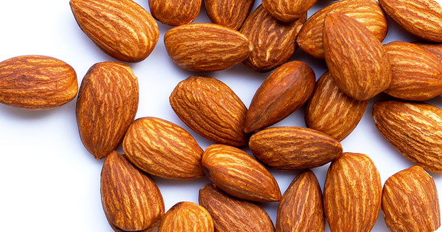 A close-up of several raw almonds with brown, textured shells, scattered on a white surface.