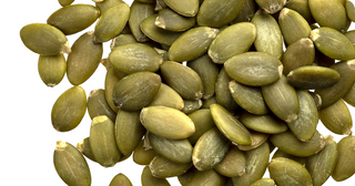 A close-up view of a pile of green pumpkin seeds, also known as pepitas, arranged densely against a white background.