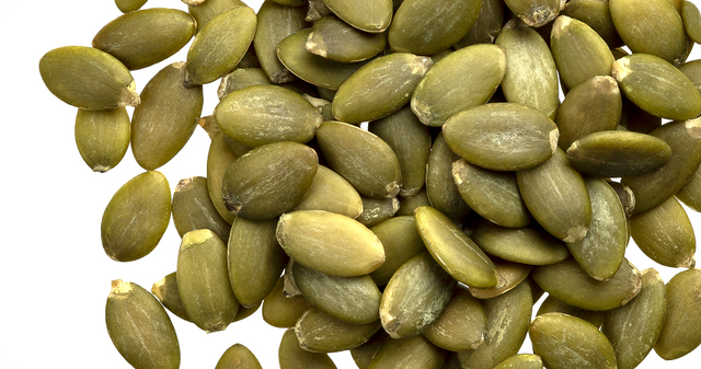 A close-up view of a pile of green pumpkin seeds, also known as pepitas, arranged densely against a white background.
