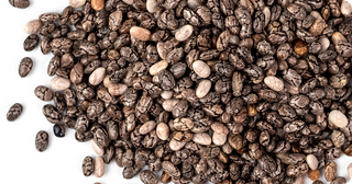 A pile of dried chia seeds, black and white in color, scattered on a white surface.