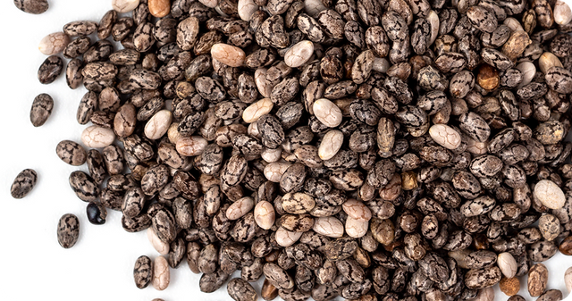 A pile of dried chia seeds, black and white in color, scattered on a white surface.