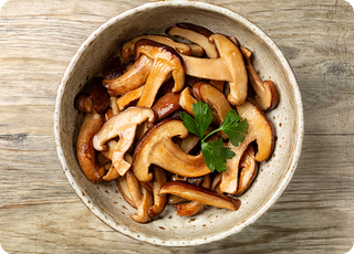 A ceramic bowl filled with cooked mushrooms garnished with fresh parsley, placed on a rustic wooden surface.