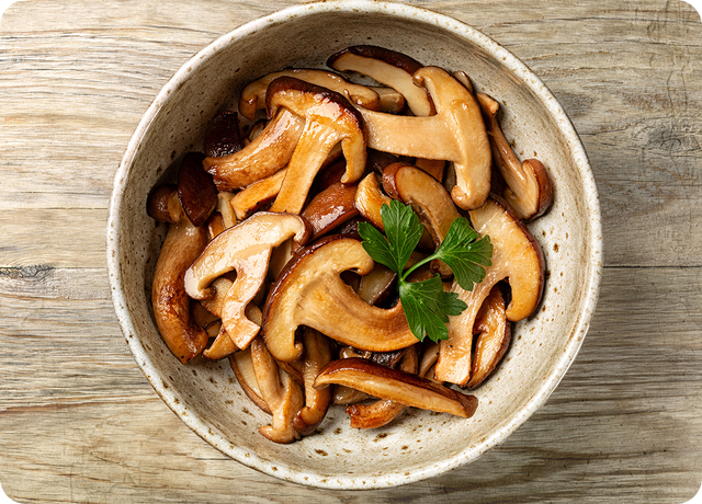 A ceramic bowl filled with cooked mushrooms garnished with fresh parsley, placed on a rustic wooden surface.