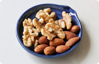 A small blue dish containing several walnut halves and whole almonds, placed on a white surface.