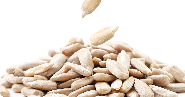 A close-up of shelled sunflower seeds piled together, with a few seeds falling from above, set against a white background.