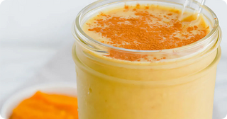 A glass of creamy orange smoothie topped with cinnamon powder, with a clear straw and a small dish of orange fruit puree in the background.