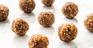 Nine round, brown energy balls with visible oat and nut pieces are arranged on a white marble surface.