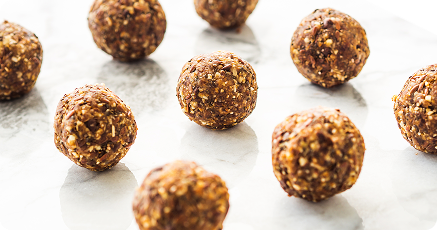 Nine round, brown energy balls with visible oat and nut pieces are arranged on a white marble surface.