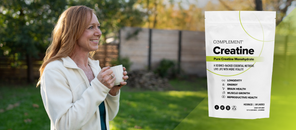 A smiling woman stands outdoors holding a mug, next to a large package of Complement Creatine Monohydrate supplement. The background features a sunny garden with trees and a wooden fence.