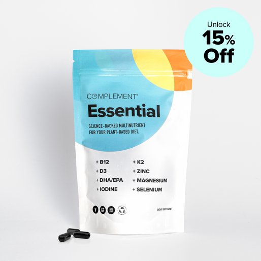 A colorful pouch labeled “Complement Essential” with a list of nutrients, including B12, D3, and zinc, stands upright. Two black capsules lie next to the pouch. A blue circle in the corner reads, “Unlock 15% Off.”.