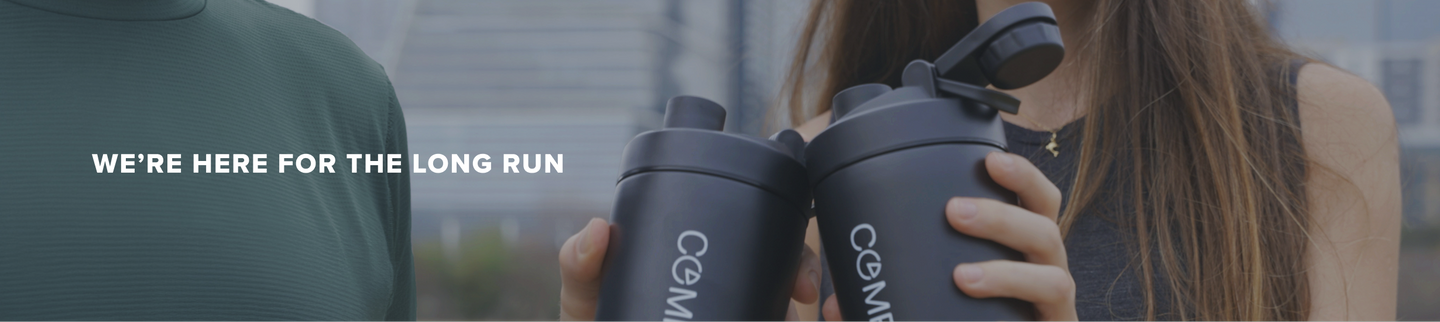 Two people are holding black shaker bottles and clinking them together. The text WERE HERE FOR THE LONG RUN is displayed on the left side of the image.