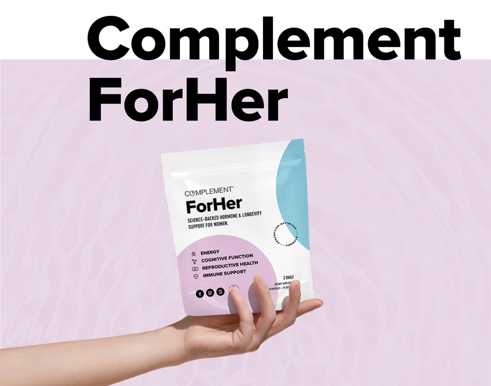 A hand holds a pouch labeled Complement ForHer against a pink background. The packaging highlights benefits like energy, digestive function, reproductive health, and immune support.