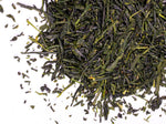 Loose green tea leaves scattered on a white background, showing their deep green color and varied shapes.