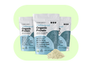 Three bags of Orgain Organic Protein powder with an unflavored label stand in front of a green background. In front of the bags, there is a small pile of protein powder.