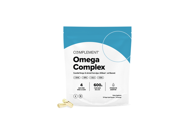 A white and blue package labeled Complement Omega Complex sits on a white background, with two yellow capsules placed in front of it.