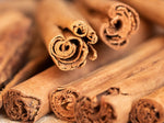 Close-up of several cinnamon sticks, showing their curled, textured bark in detail. The sticks are brown and arranged in a slightly overlapping manner.