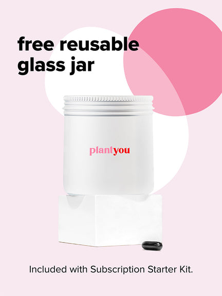 A white glass jar with Plant You text sits atop a small white block against a background with overlapping pink and white circles. A black capsule is positioned near the jar. Text reads free reusable glass jar and Included with Subscription Starter Kit.