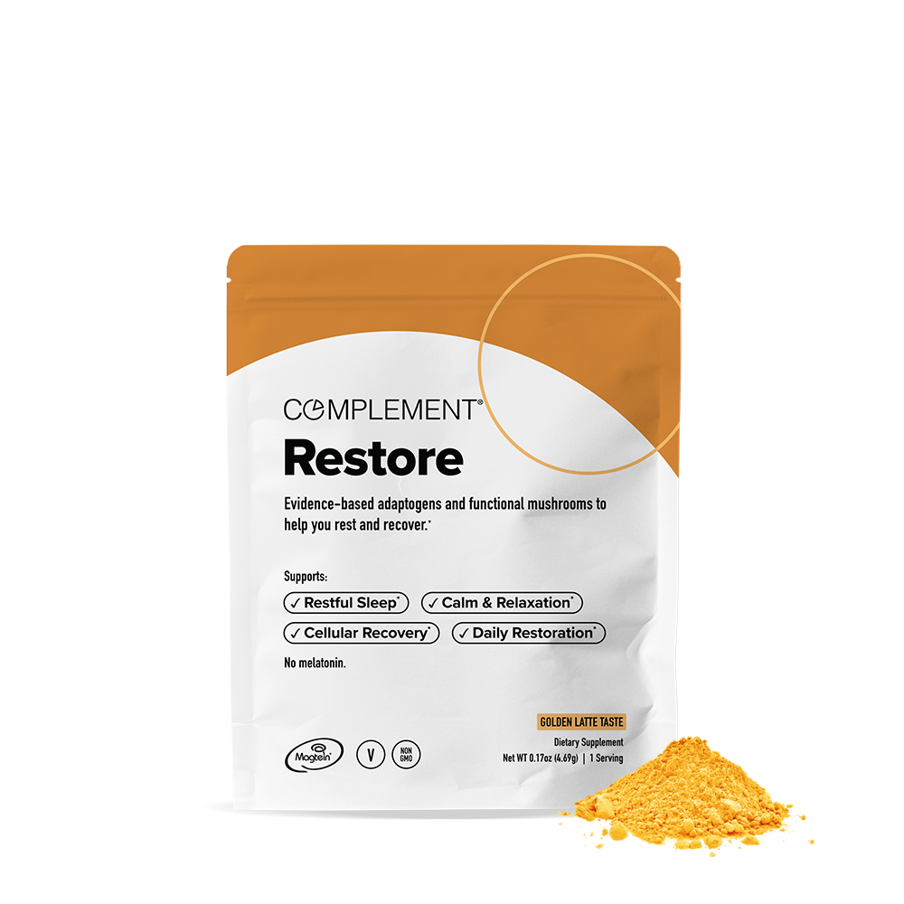 A white and orange packet labeled Complement Restore, featuring text about adaptogens and mushrooms for rest and recovery, with a serving of golden powder displayed beside the packet.