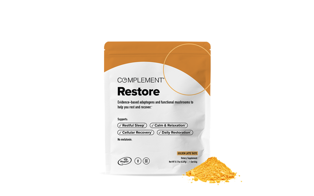 A white and orange bag labeled Complement Restore stands next to a small pile of yellow-orange powder. The bag highlights benefits like restful sleep, relaxation, cellular recovery, and daily restoration.