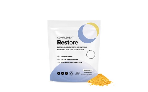 A white and blue pouch labeled Complement Restore stands upright next to a small pile of yellow powder. The packaging highlights benefits like deeper sleep, cellular recovery, and stronger rejuvenation.