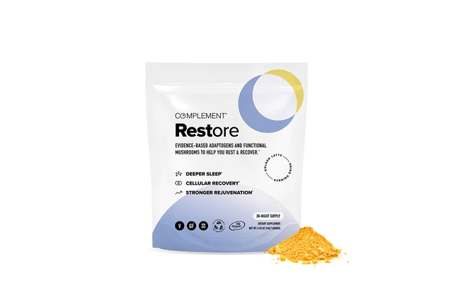 A white and blue pouch labeled Complement Restore stands upright next to a small pile of yellow powder. The packaging highlights benefits like deeper sleep, cellular recovery, and stronger rejuvenation.