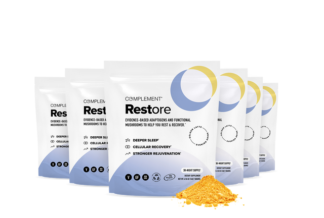 Six white and blue pouches labeled Complement Restore are arranged in a row with a yellow powder spilled in front. The packaging highlights benefits like deeper sleep, cellular recovery, and stronger rejuvenation.