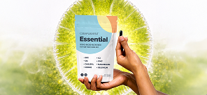 A person holds a packet labeled Essential and a black capsule against a bright, green, sunburst-like background suggesting health and vitality.