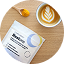 A packet labeled Complement Restore, a spoonful of yellow powder, and a cup of latte with leaf-shaped foam art are arranged on a wooden table.