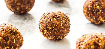 Close-up of several round, textured energy bites made with oats, seeds, and dried fruit, arranged on a white marble surface.
