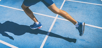 Runner in blue shoes sprinting on a blue track, with only their legs visible and casting a shadow beside white lane lines.