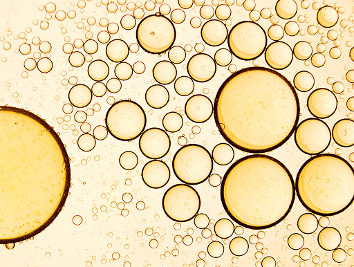 Close-up of numerous yellow and brown oil droplets of various sizes suspended in water, creating a bubble-like pattern against a light background.