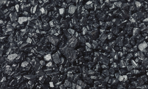 A close-up view of a pile of small, shiny black coal or charcoal pieces with rough and uneven surfaces.