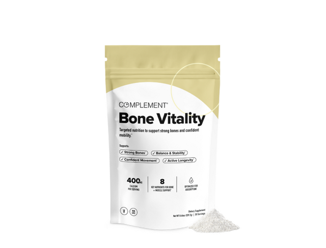 A package labeled Complement Bone Vitality dietary supplement stands upright with some white powder spilled beside it on a white background.