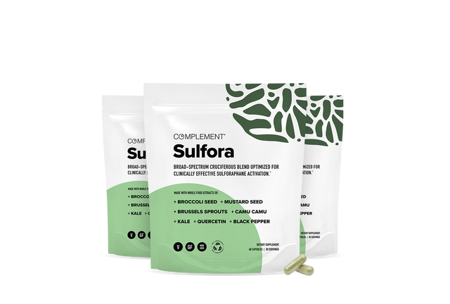 Three white and green supplement pouches labeled Complement Sulfora stand upright, with two yellow capsules placed in front. The pouches feature green leaf patterns and list ingredients like broccoli seed and kale.