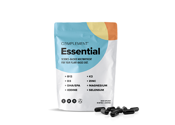 A standing pouch of Complement Essential, a plant-based multinutrient supplement, is shown. The package lists nutrients like B12, D3, DHA/EPA, iodine, K2, zinc, magnesium, and selenium. Black capsules are scattered in front of the pouch.