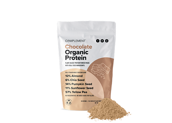 A package of Complement Chocolate Organic Protein is shown. The front lists ingredients: almond, chia seed, pumpkin seed, sunflower seed, and yellow pea. A small pile of protein powder is beside the bag.