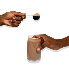 Two hands are pictured on a white background. One holds a glass of chocolate milk, while the other holds a spoon with chocolate powder above the glass.