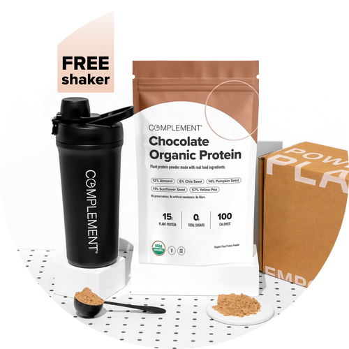 A bag of Complement Chocolate Organic Protein powder, a black shaker, a scoop of powder, and a box. Text reads FREE shaker. The bag lists plant-based ingredients and nutritional info.
