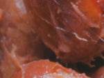 Close-up view of reddish, glossy, textured surfaces that appear organic, possibly raw meat or a fruit with a fibrous texture and some shiny, moist areas.