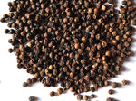 A close-up of a large pile of whole black peppercorns scattered on a white surface.