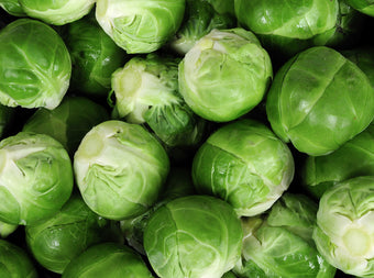 A close-up view of several fresh, green Brussels sprouts, tightly packed together, showing their leafy layers and vibrant color.